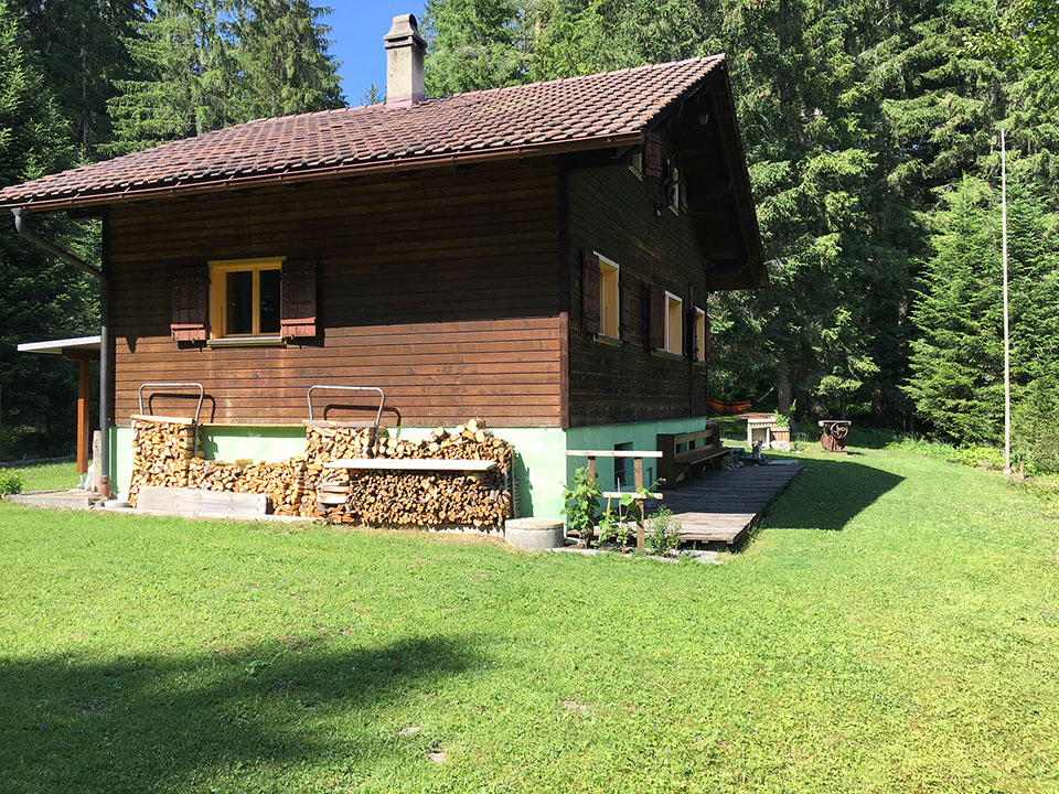 Die Stube des Waldfrieden Ferienhauses verfügt über einen grossen Holztisch und eine Eckbank sowie ein rotes Sofa.